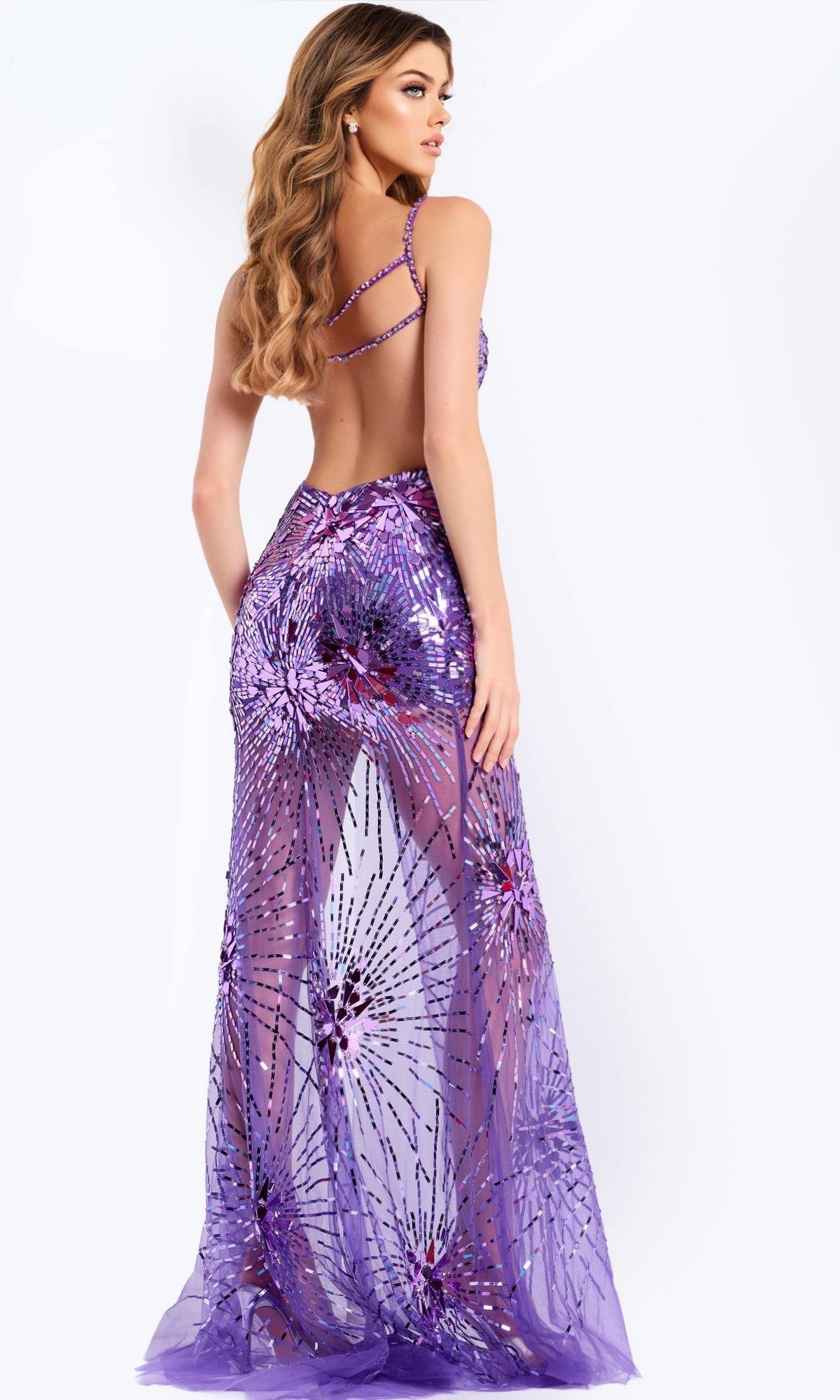 A woman with long wavy hair models the Jovani 48502, a sleeveless, backless long prom dress with a floor-length sheath skirt and sheer sequined floral pattern, standing against a plain background.